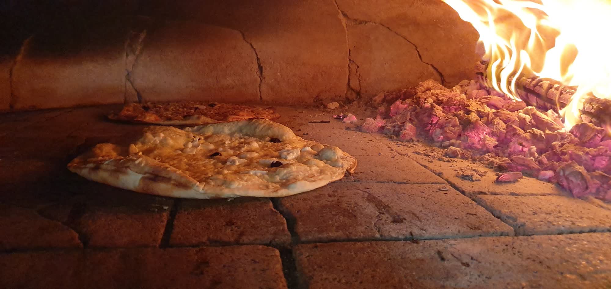 L'intérieur du four à bois du camion Chez Cyril à Ajaccio : pizzas sur la sole, braises et bois en flammes